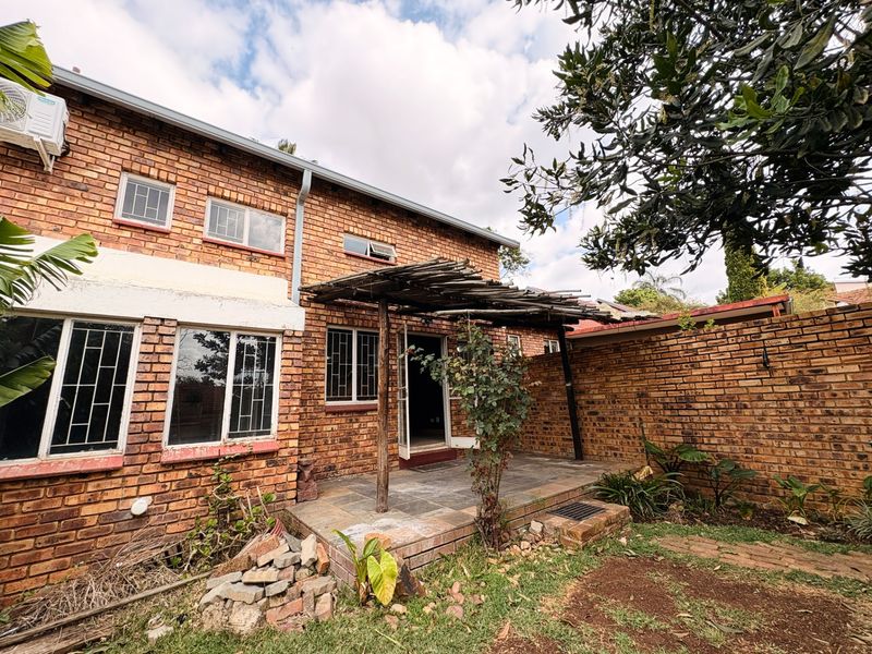 Rear exterior view of a brick townhouse featuring a slate patio, timber pergola, and security-fitted windows, set against a private garden area.