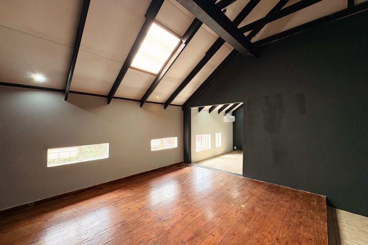 Spacious living area featuring vaulted ceilings with exposed beams, a skylight, hardwood flooring, and an adjoining tiled space with air conditioning.