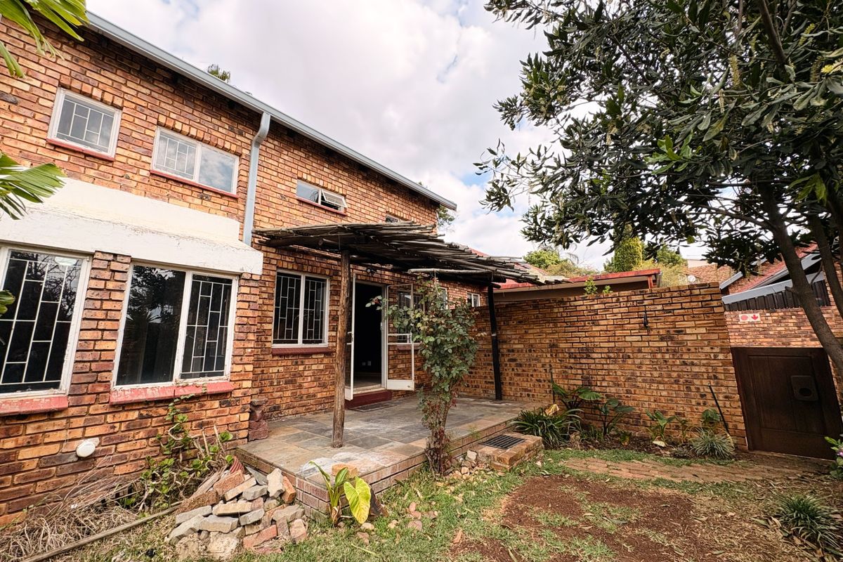 Rear exterior view of a face brick townhouse featuring a slate patio, timber pergola, and enclosed garden area with boundary wall.