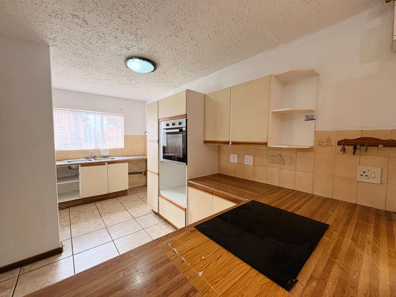A dated kitchen featuring built-in cabinetry, an integrated oven, electric hob, and tiled flooring, offering significant potential for a modern renovation.