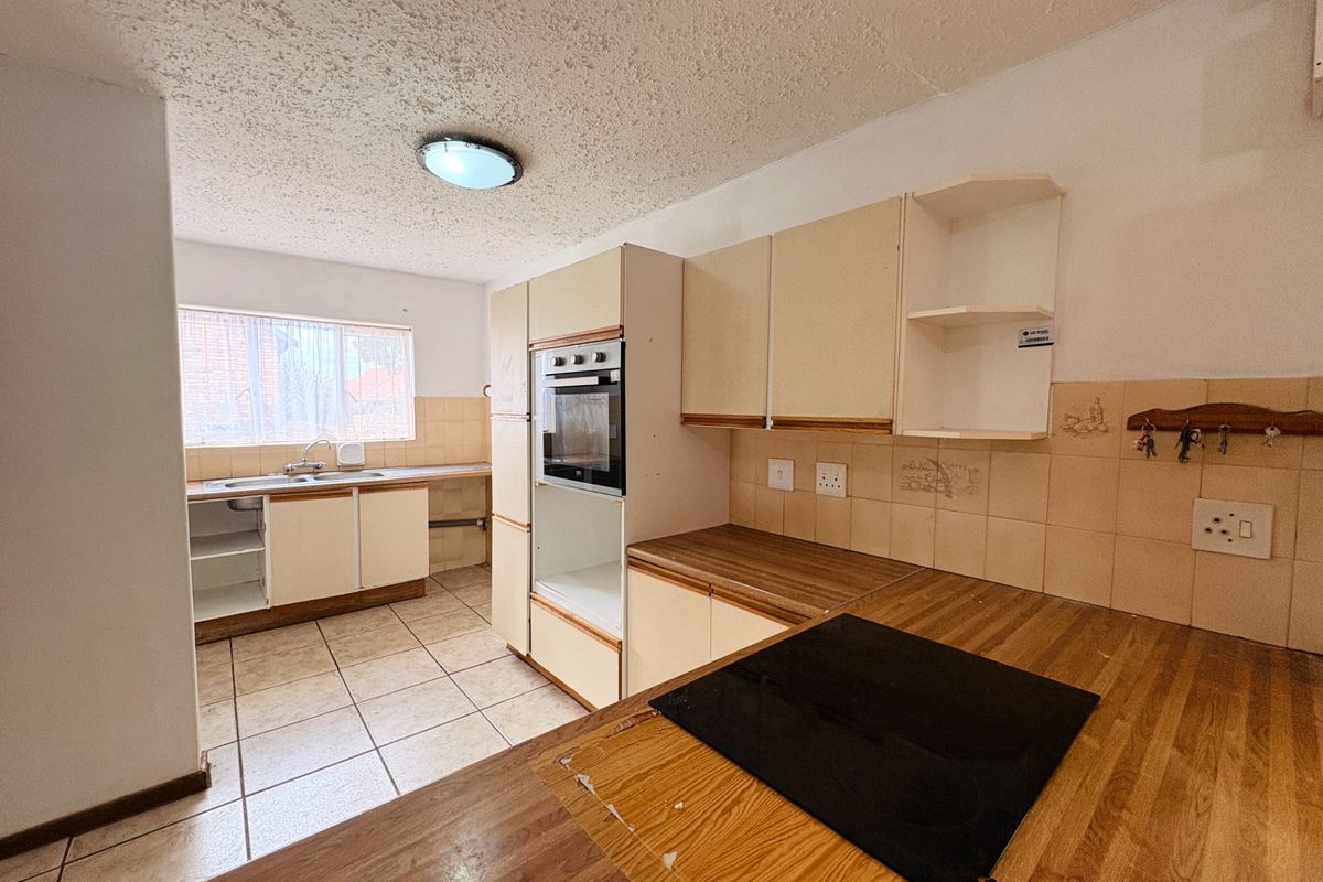 A dated kitchen featuring built-in cabinetry, an integrated oven, electric hob, and tiled flooring, offering significant potential for a modern renovation.