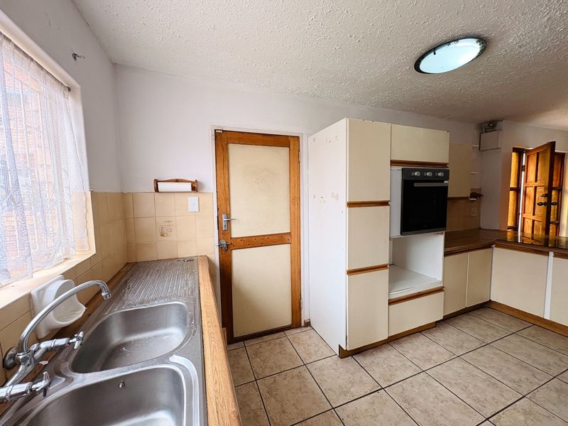 A dated kitchen featuring built-in cabinetry, a double bowl stainless steel sink, and a built-in oven, offering significant potential for modernization and renovation.