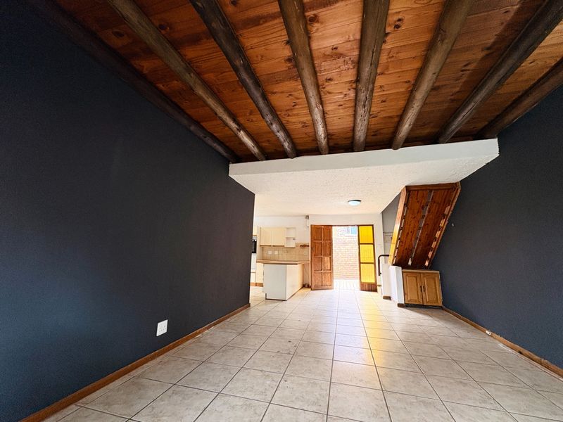 Open plan living area featuring exposed timber beam ceilings, tiled flooring, and direct access to the rear exterior through a timber door.