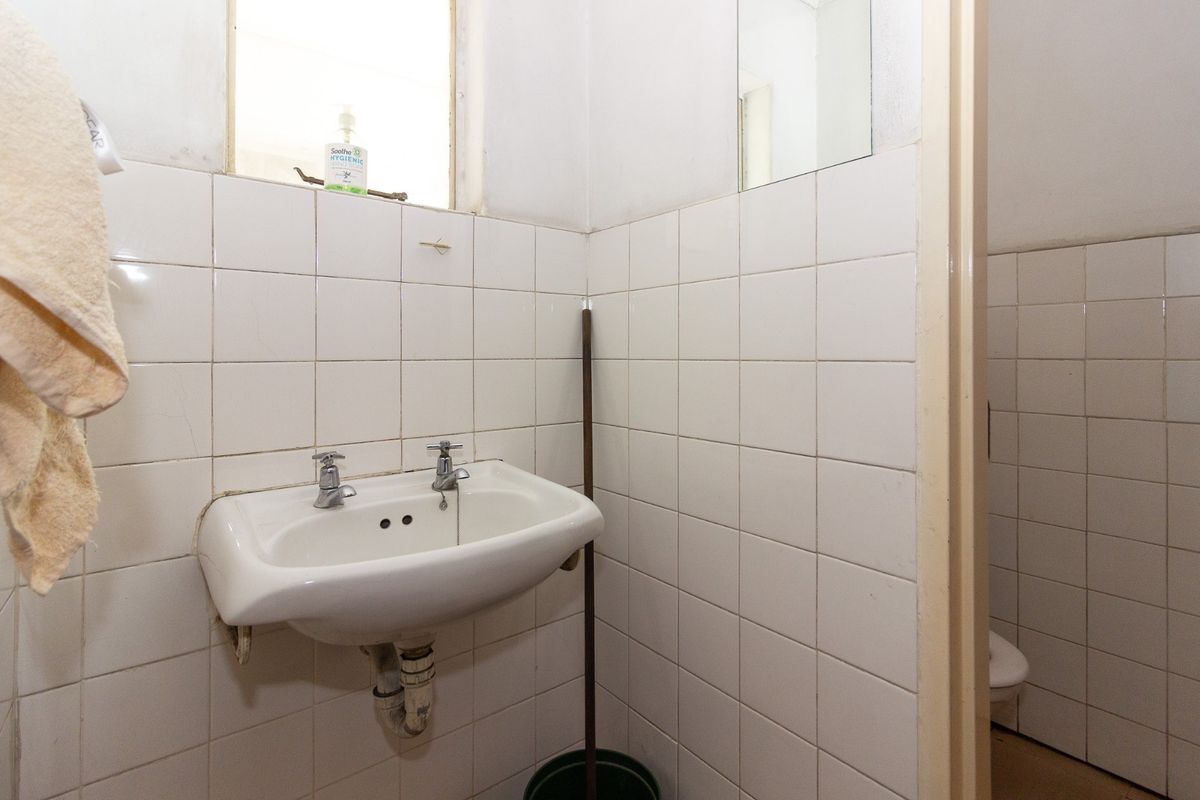 A functional bathroom featuring a wall-mounted ceramic basin with dual-handle taps and white wall tiling, requiring cosmetic updates to improve its overall condition.