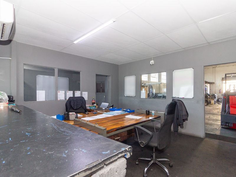 Functional industrial office space featuring internal glass partitions, drop ceiling, air conditioning, and a built-in service counter with direct access to the warehouse area.
