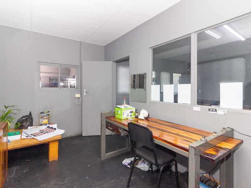 Functional industrial office space featuring a glass partition, drop ceiling, and durable flooring, suitable for administrative or operational use.