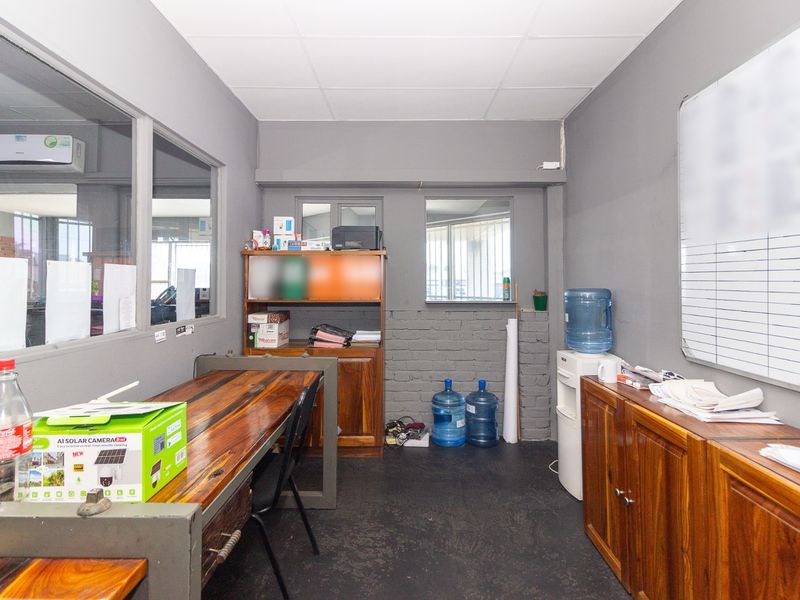 A functional office space featuring internal glass partitioning, exposed brick accents, and built-in storage cabinetry, suitable for a professional industrial work environment.