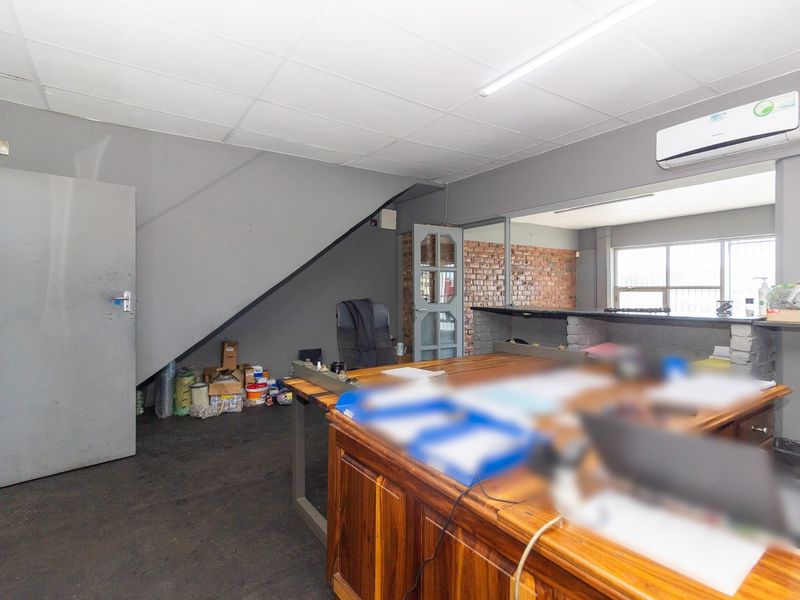 Functional industrial office space featuring exposed brick accents, a suspended ceiling, and a wall-mounted air conditioning unit.