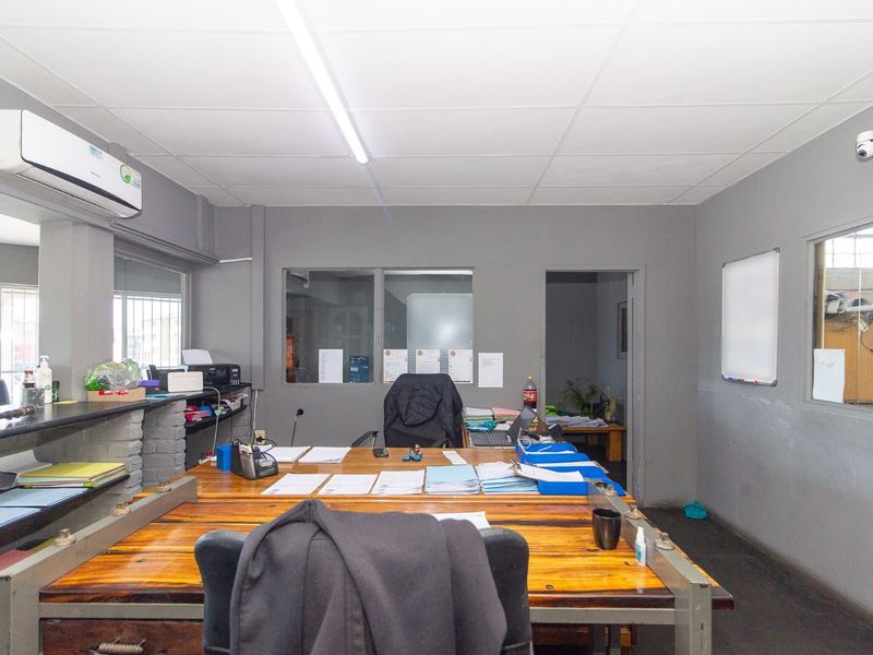 Functional industrial office space featuring internal glass partitions, split-system air conditioning, and overhead fluorescent lighting.