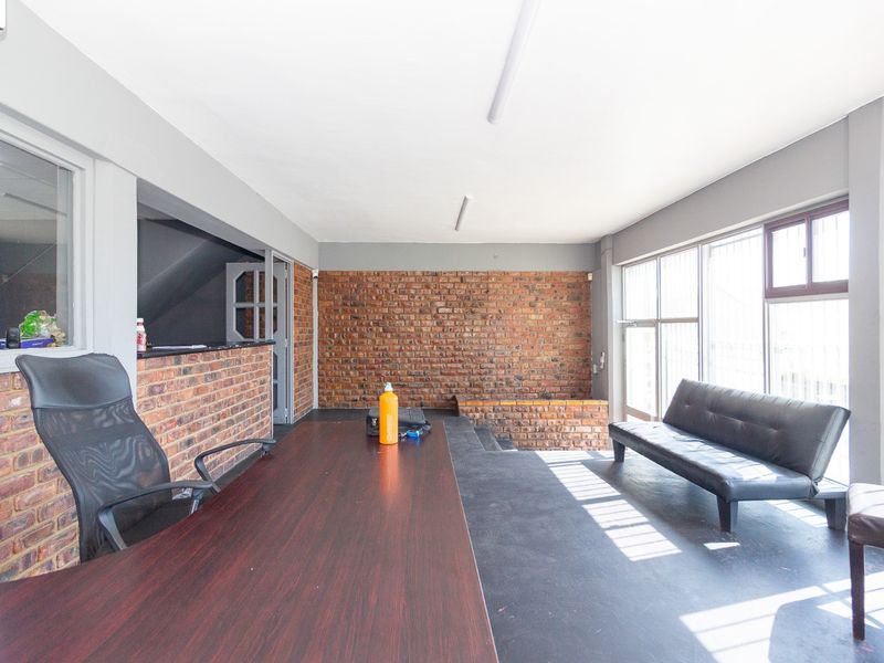 A spacious office area featuring exposed brick walls, large windows providing natural light, and a raised platform section.