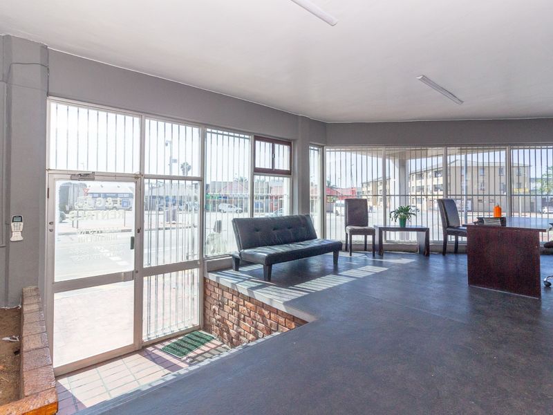 Industrial entry area featuring large aluminum-framed windows with security bars, brick detailing, and durable flooring, suitable for a reception or office space.