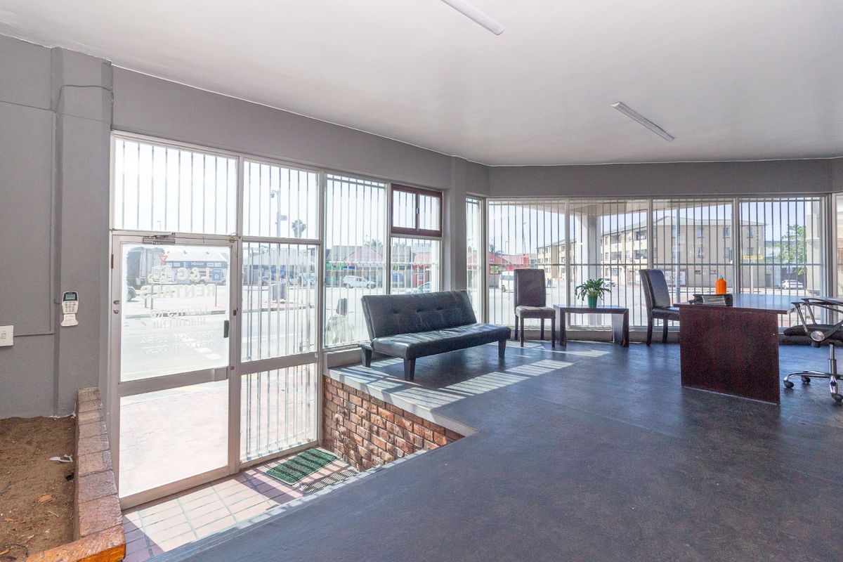 Industrial entry area featuring large aluminum-framed windows with security bars, brick detailing, and durable flooring, suitable for a reception or office space.