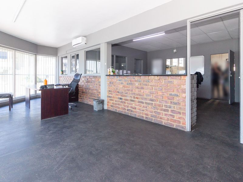 A functional industrial office space featuring exposed brick accents, a built-in reception counter, and large windows with security bars.