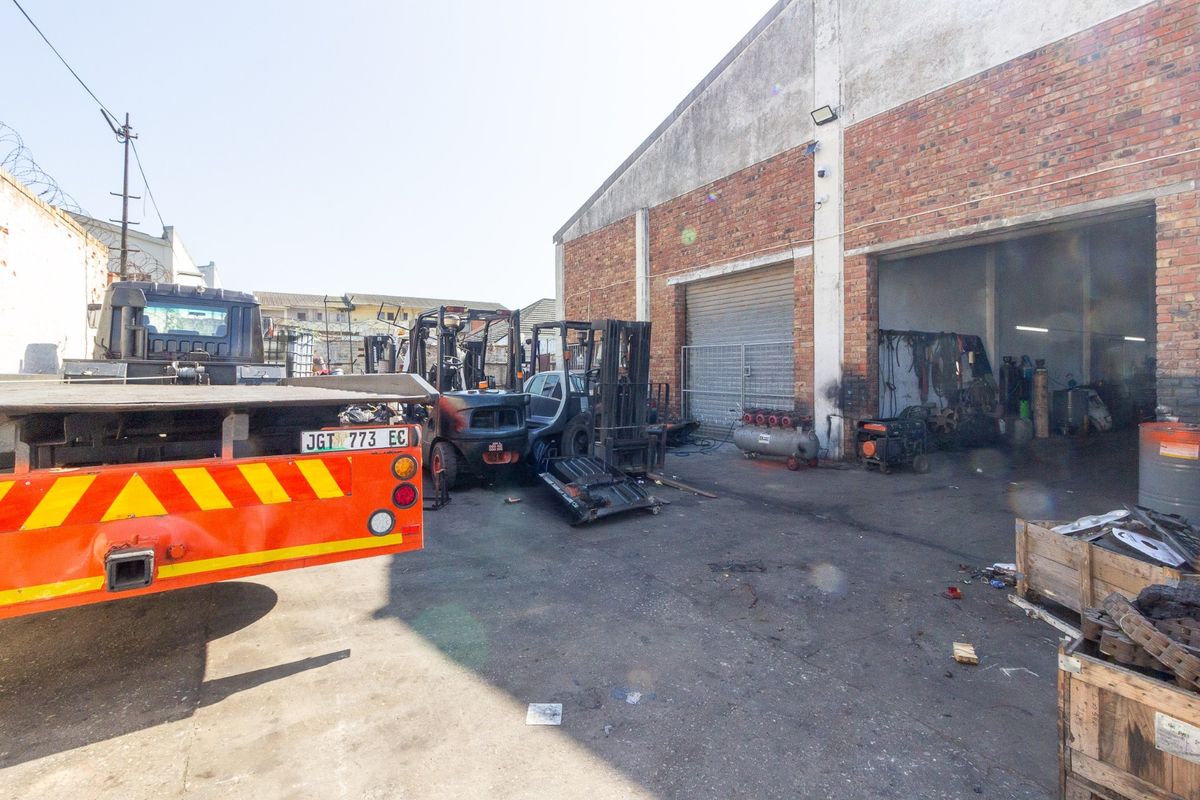 Industrial rear yard area featuring a brick facade, roller shutter access, and concrete hardstanding suitable for heavy vehicle operations.