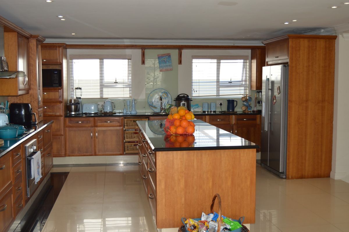 Spacious kitchen featuring warm-toned wooden cabinetry, a large central island with granite countertops, integrated appliances, and polished tiled flooring.