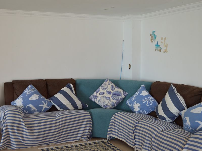 A living room area featuring coving and recessed ceiling lighting, currently styled with a large corner sofa.