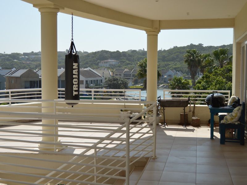 Spacious covered balcony featuring tiled flooring, structural columns, and a metal balustrade, offering scenic views of the surrounding estate and water.