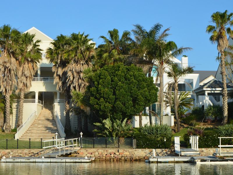 Rear view of a multi-level waterfront property featuring a private jetty, stone retaining wall, and expansive staircase leading to the residence.