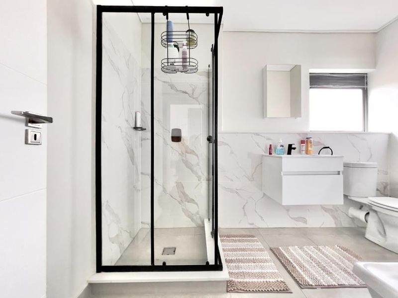 Modern bathroom featuring a walk-in shower with black frame, marble-look wall tiles, and a sleek wall-mounted vanity.