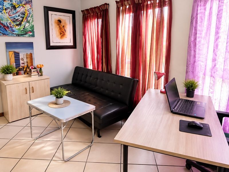 A functional living area featuring tiled flooring and large windows, providing a versatile space suitable for a lounge or home office setup.