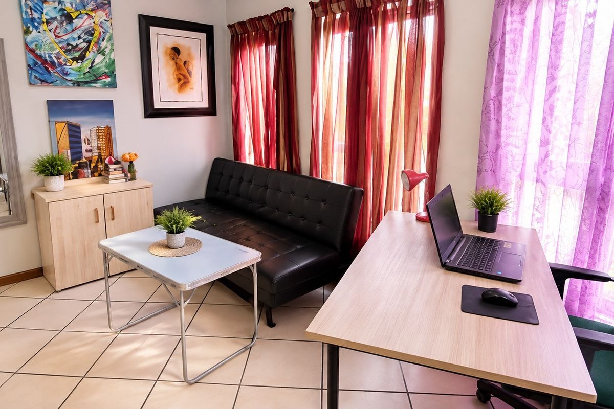 A functional living area featuring tiled flooring and large windows, providing a versatile space suitable for a lounge or home office setup.