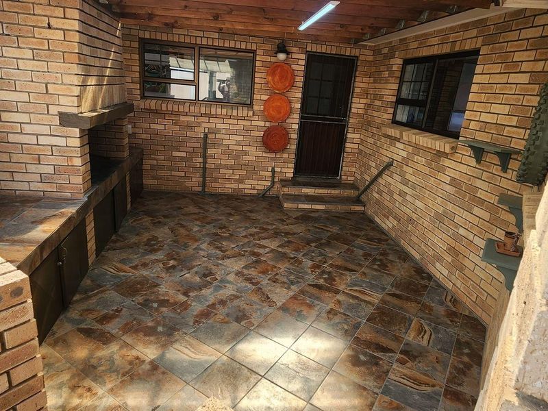Covered outdoor patio area featuring a built-in brick braai, tiled flooring, and exposed timber ceiling beams, providing a functional space for outdoor entertaining.