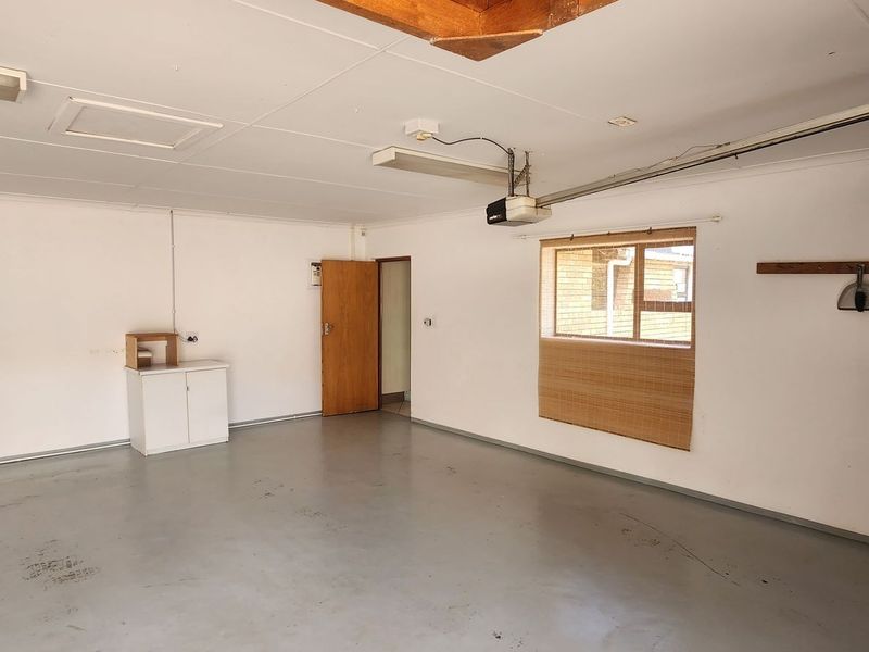 A spacious, empty garage featuring a painted concrete floor, overhead lighting, and a functional garage door motor.