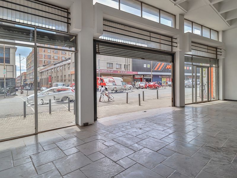Spacious open-plan commercial retail unit featuring large glass storefront windows, tiled flooring, and high ceilings with exposed structural beams, offering excellent street visibility.