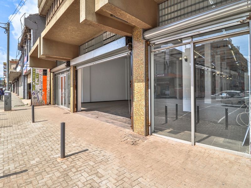 Commercial storefront featuring a large glass display window and a roller shutter door, situated on a paved street-level sidewalk.