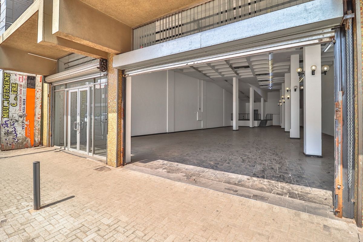 Commercial storefront featuring a large roller shutter door, glass entrance, and an open-plan interior with concrete columns and tiled flooring.