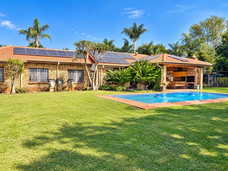 Spacious rear garden featuring a swimming pool, covered patio with built-in braai, and a brick house exterior equipped with solar panels.
