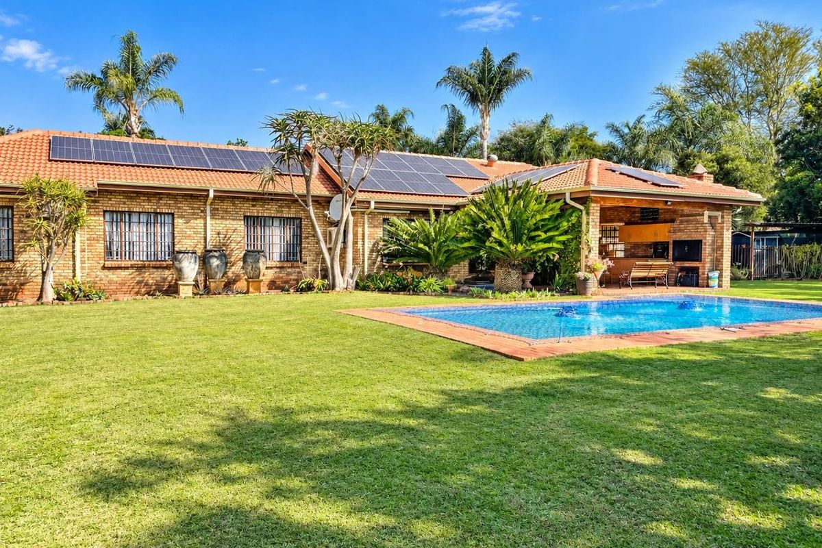 Spacious rear garden featuring a swimming pool, covered patio with built-in braai, and a brick house exterior equipped with solar panels.