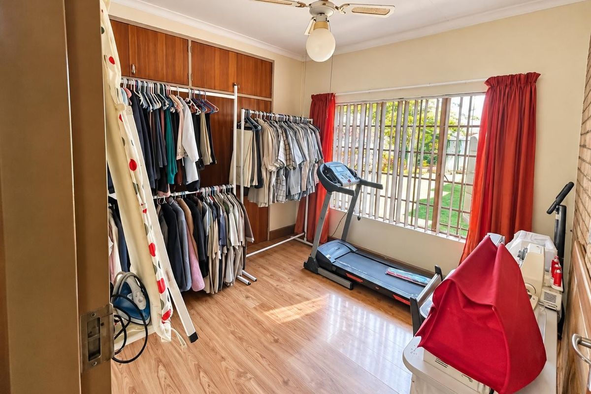 A bedroom featuring laminate flooring, built-in wooden cupboards, and a ceiling fan, currently utilized as a multi-purpose dressing and exercise room.