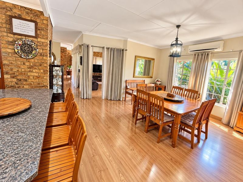Spacious open-plan dining and kitchen area featuring laminate flooring, an exposed brick feature wall, and a granite breakfast bar with integrated lighting.