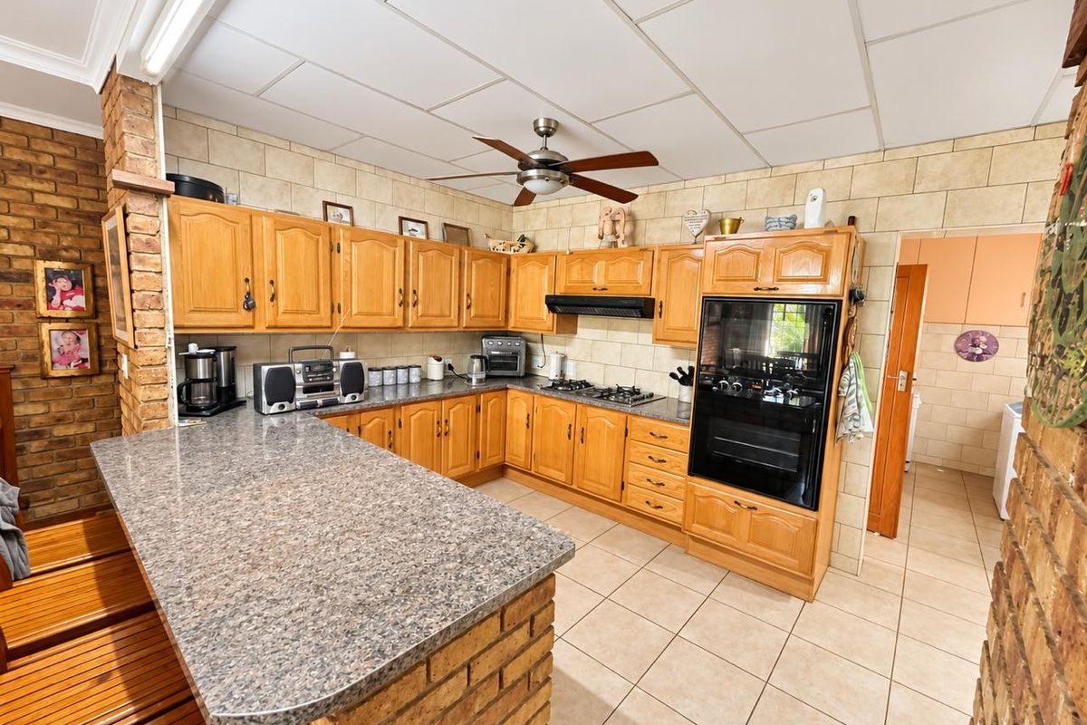 A functional kitchen featuring wooden cabinetry, a brick breakfast bar, built-in oven, gas hob, and tiled finishes throughout.