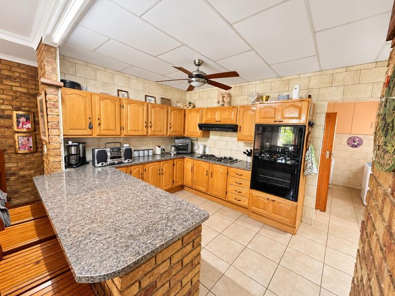 A functional kitchen featuring wooden cabinetry, a brick breakfast bar, built-in oven, gas hob, and tiled finishes throughout.