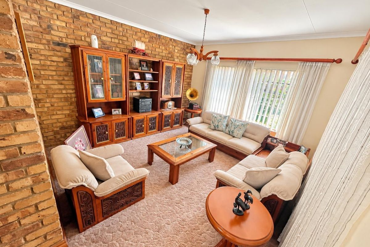 A spacious living room featuring a prominent exposed brick wall, neutral carpeting, and large windows with curtain tracks, offering a classic and comfortable layout.
