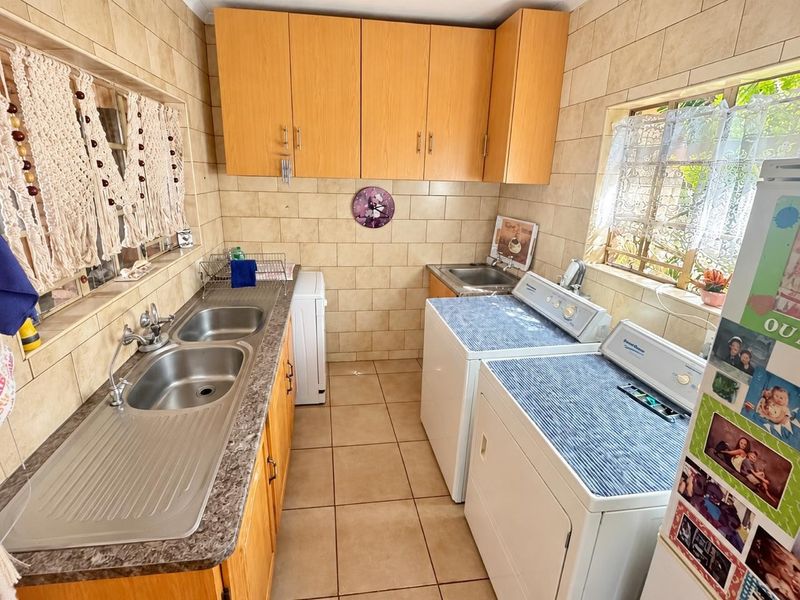 Functional laundry room featuring double and single stainless steel sinks, ample wooden cabinetry, laminate countertops, and durable ceramic tile flooring throughout.