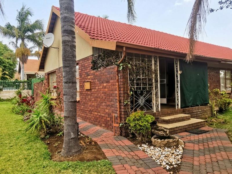 A side view of a face-brick house featuring a tiled roof, paved walkway, and established garden surroundings.