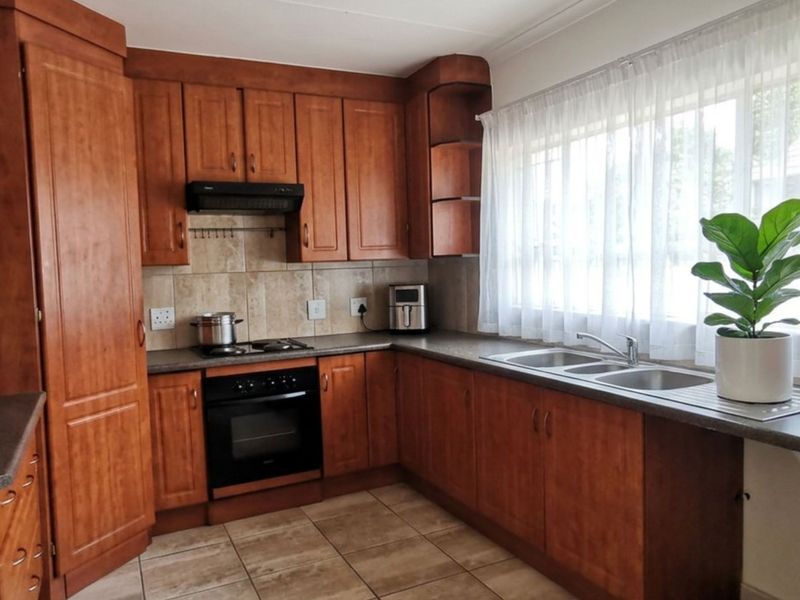A functional kitchen featuring warm-toned wooden cabinetry, tiled backsplash, built-in oven with gas hob, and a double bowl sink under a large window.