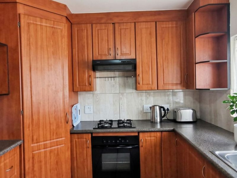 A functional kitchen featuring warm-toned wooden cabinetry, dark laminate countertops, a built-in oven with gas hob, and a stainless steel sink.