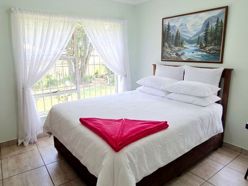 A functional bedroom featuring tiled flooring, a built-in cupboard, and a window fitted with security bars overlooking the garden.