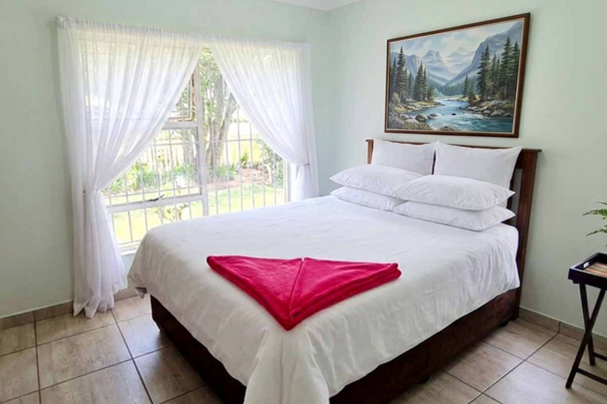 A functional bedroom featuring tiled flooring, a built-in cupboard, and a window fitted with security bars overlooking the garden.