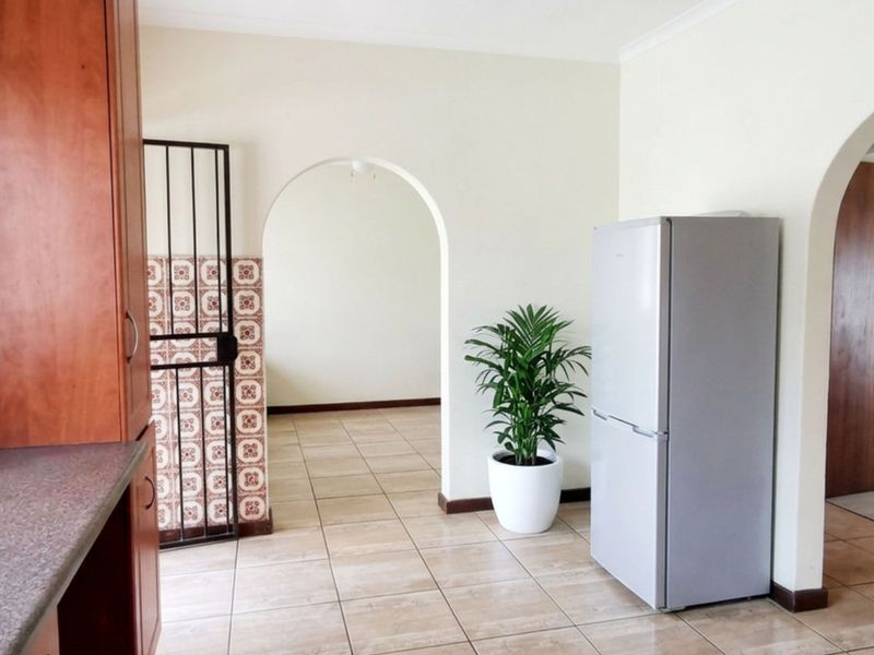 A functional kitchen area featuring built-in wooden cabinetry, laminate countertops, and ceramic floor tiles, connected to adjacent living spaces via classic archways.
