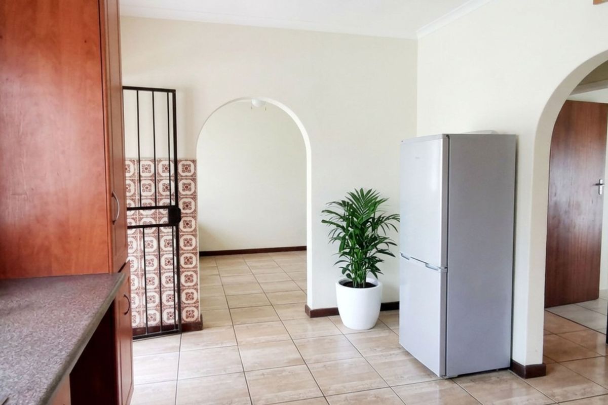 A functional kitchen area featuring built-in wooden cabinetry, laminate countertops, and ceramic floor tiles, connected to adjacent living spaces via classic archways.