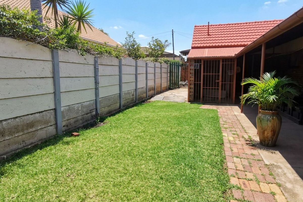 A private rear garden featuring a lawn, brick paved walkway, and a covered patio area enclosed by a precast concrete boundary wall.