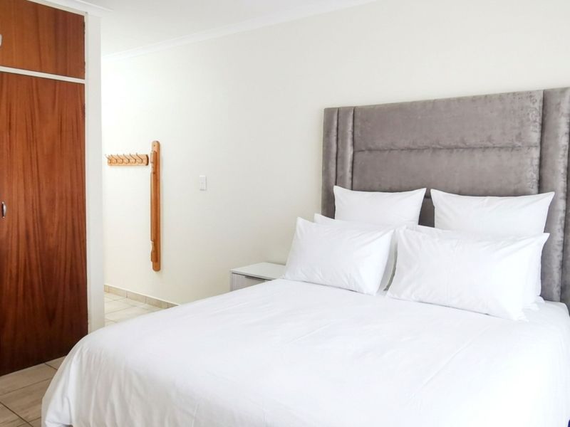 A bedroom featuring tiled flooring and a large built-in wooden wardrobe with overhead storage.