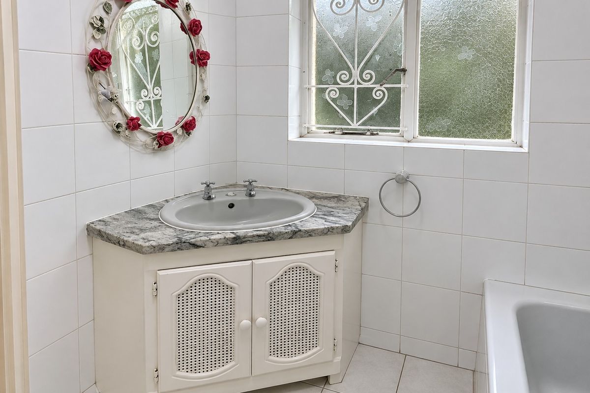 A functional bathroom featuring a corner vanity with a stone countertop, tiled walls and flooring, and a bathtub with a security-grille window.
