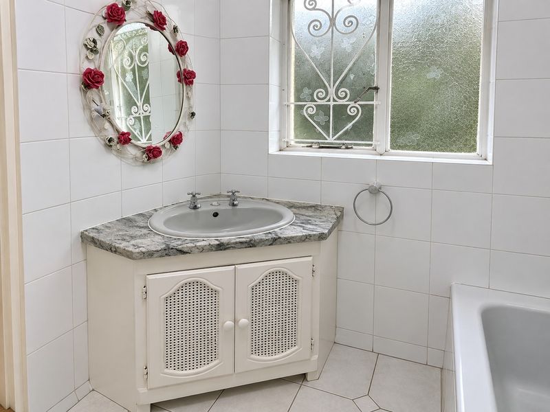 A functional bathroom featuring a corner vanity with a stone countertop, tiled walls and flooring, and a bathtub with a security-grille window.