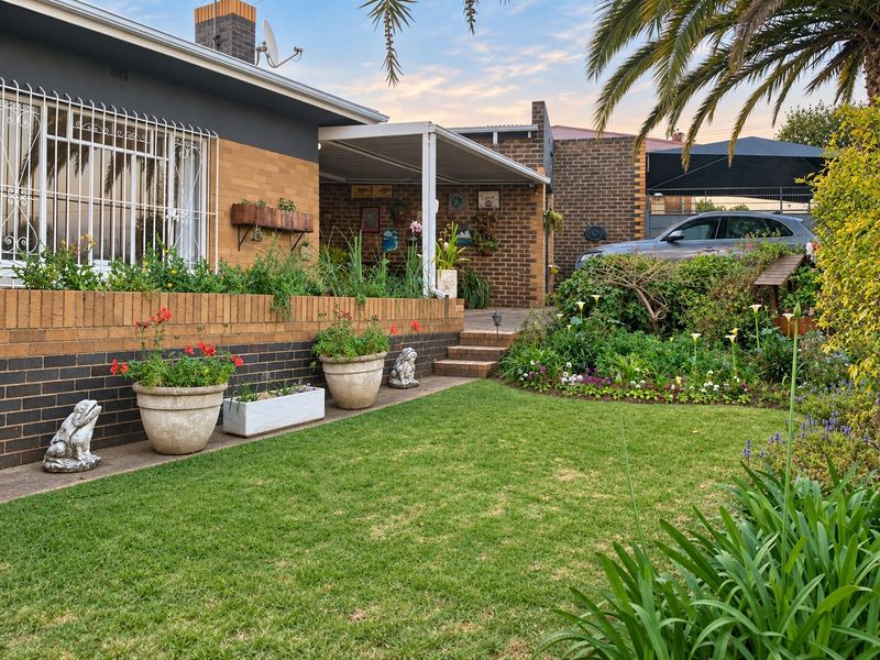A well-maintained rear garden featuring a brick facade, a covered patio area, and a neatly landscaped lawn with established garden beds.